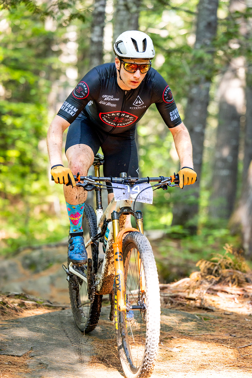 Mud-splattered racer riding over rocks on a forest trail