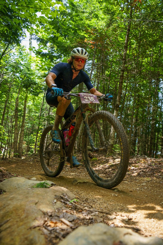 Mud-splattered racer riding over rocks on a forest trail